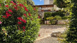 Un jardin avec des fleurs rouges, un sentier en pierre et un bâtiment à la façade en pierre.
