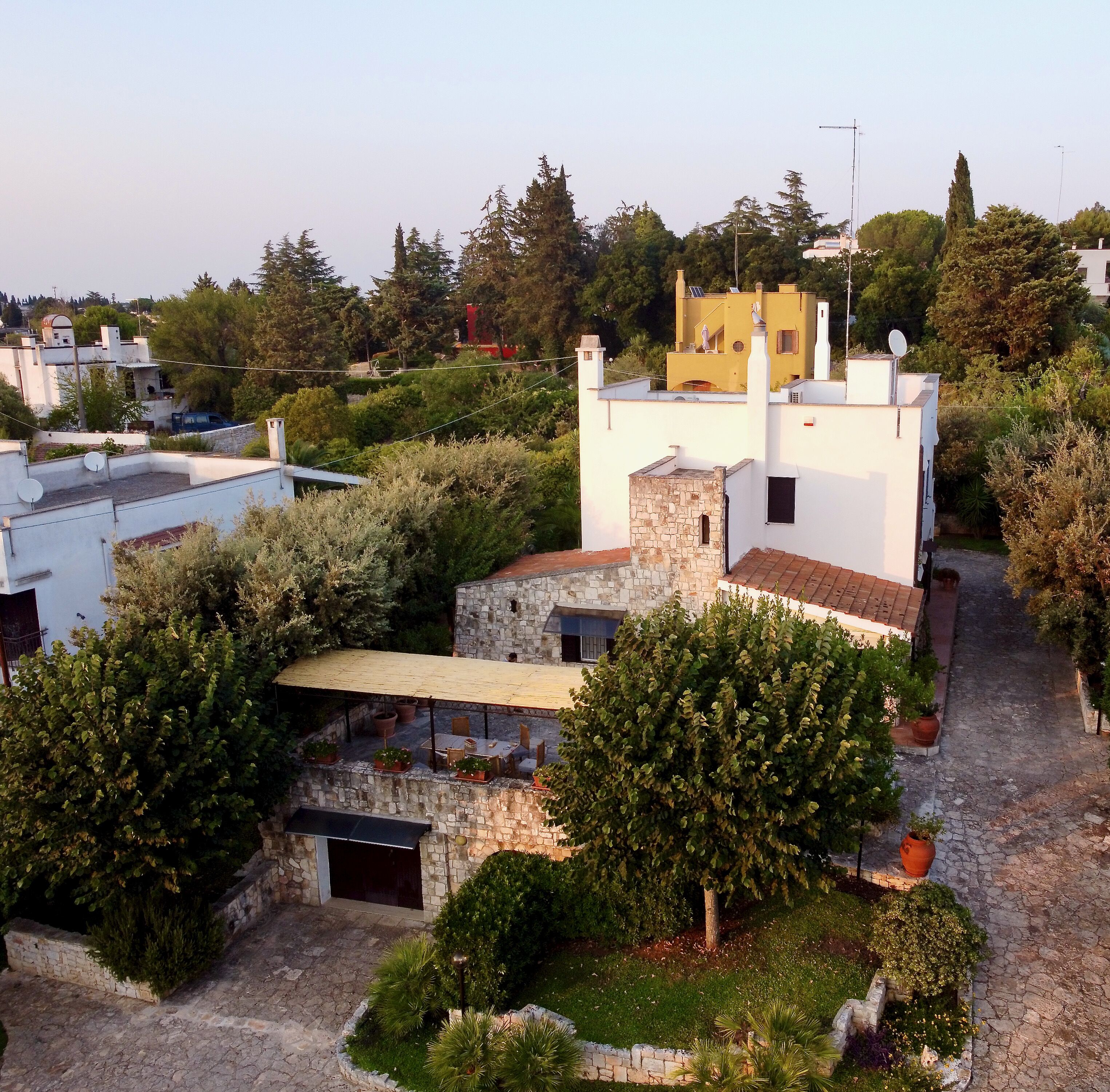 Un edificio bianco con struttura in pietra, circondato dal verde e da altri edifici.