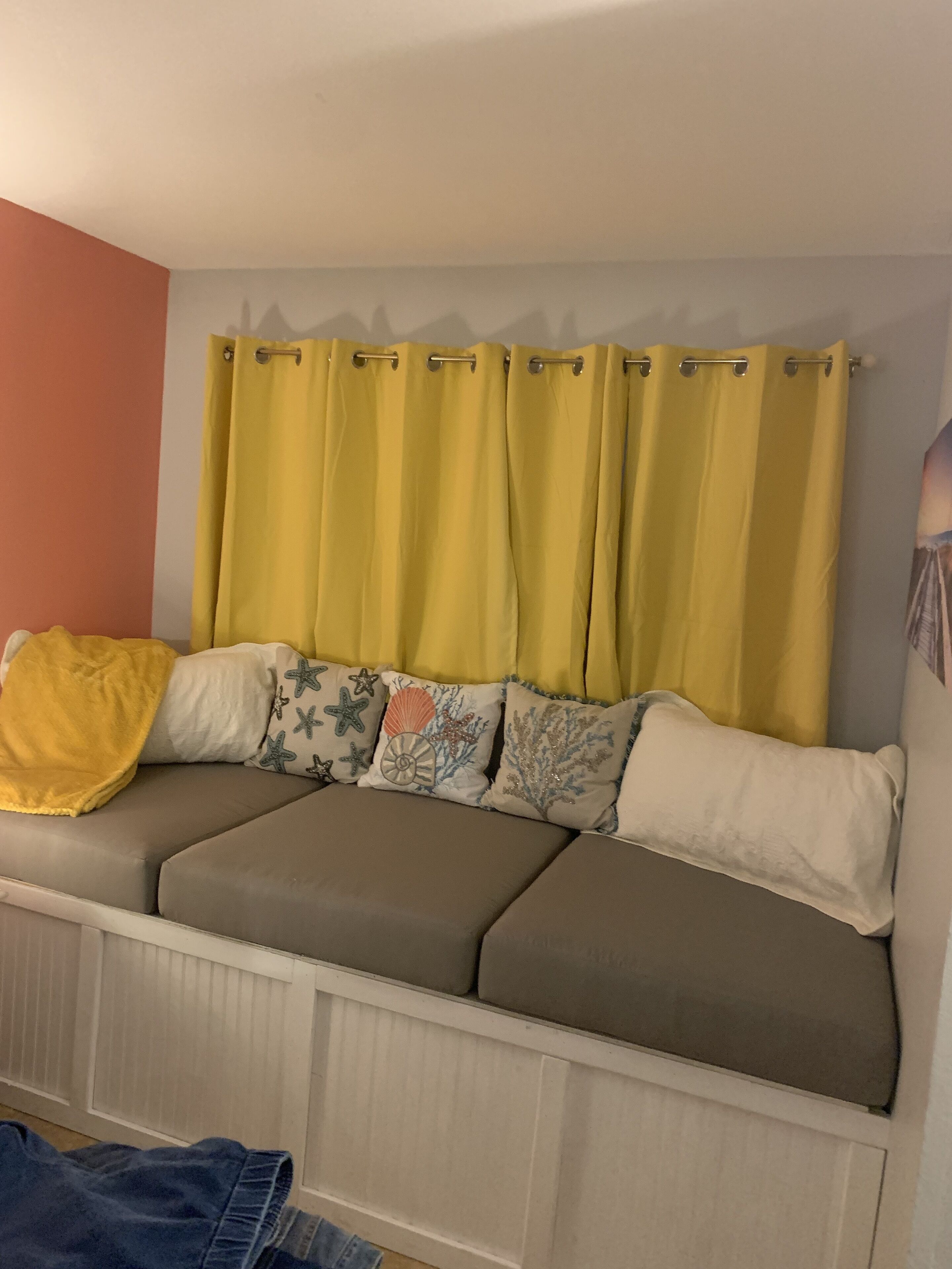 A room with a window covered by yellow curtains, a sofa with decorative pillows, and a radiator below.