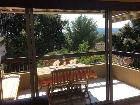 A balcony with a table set for two, overlooking a scenic view of trees and a distant landscape.