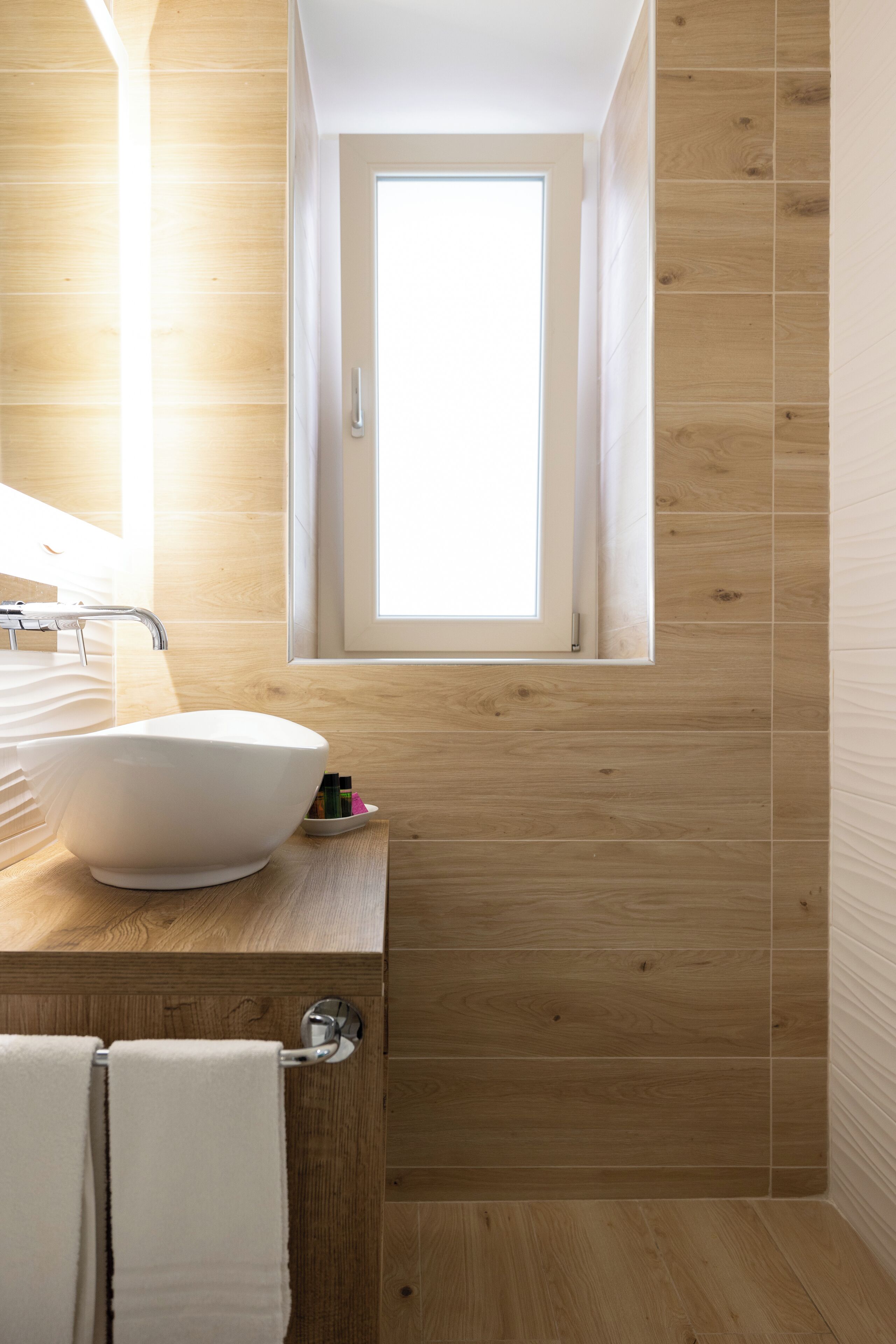 A modern bathroom with a wooden floor, a white sink, and a window above the sink.