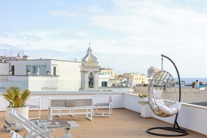 Una terraza en la azotea con muebles blancos, una silla colgante y vistas de la ciudad.