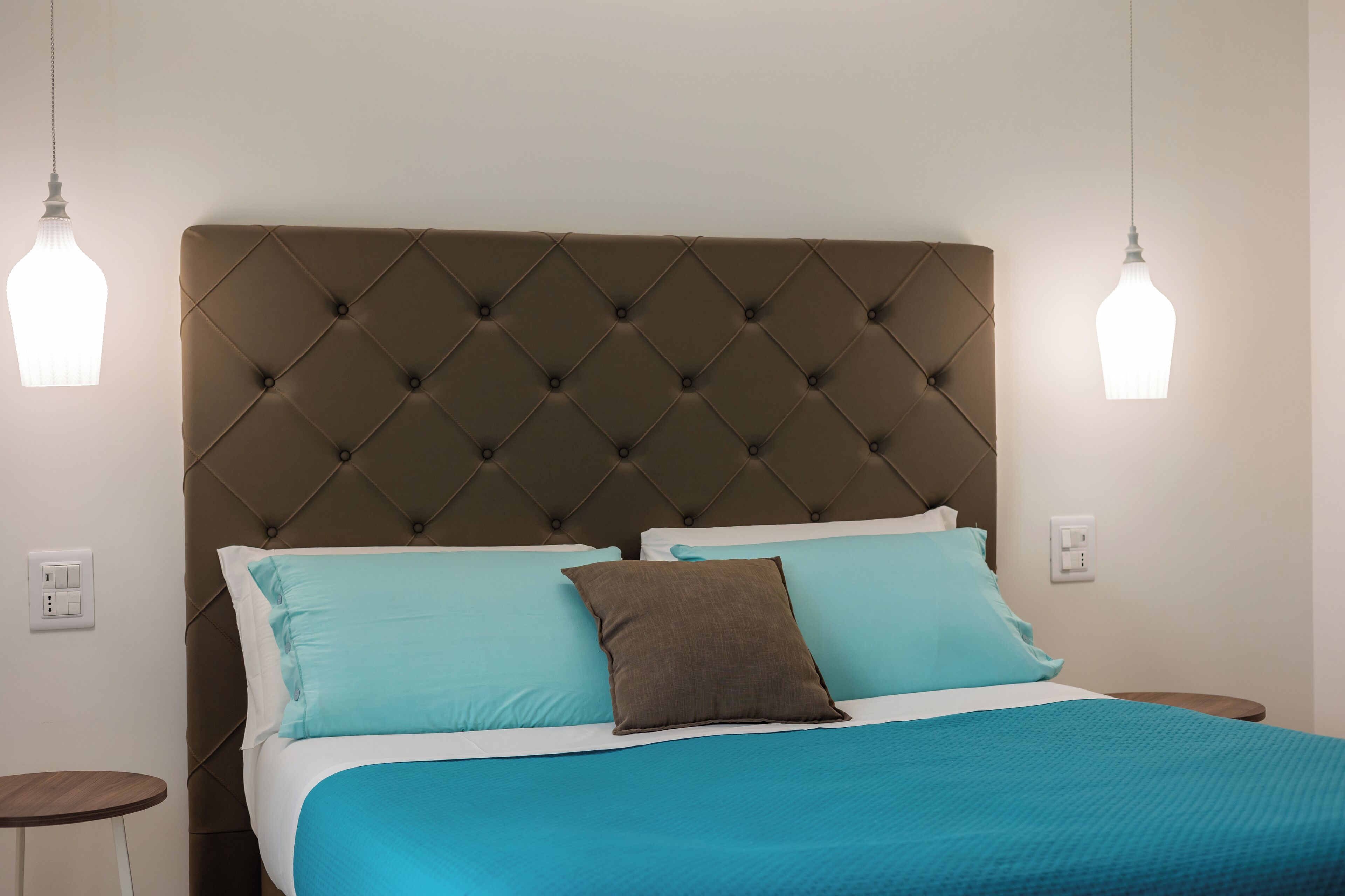 A neatly made bed with a tufted headboard, two bedside tables, and pendant lights.