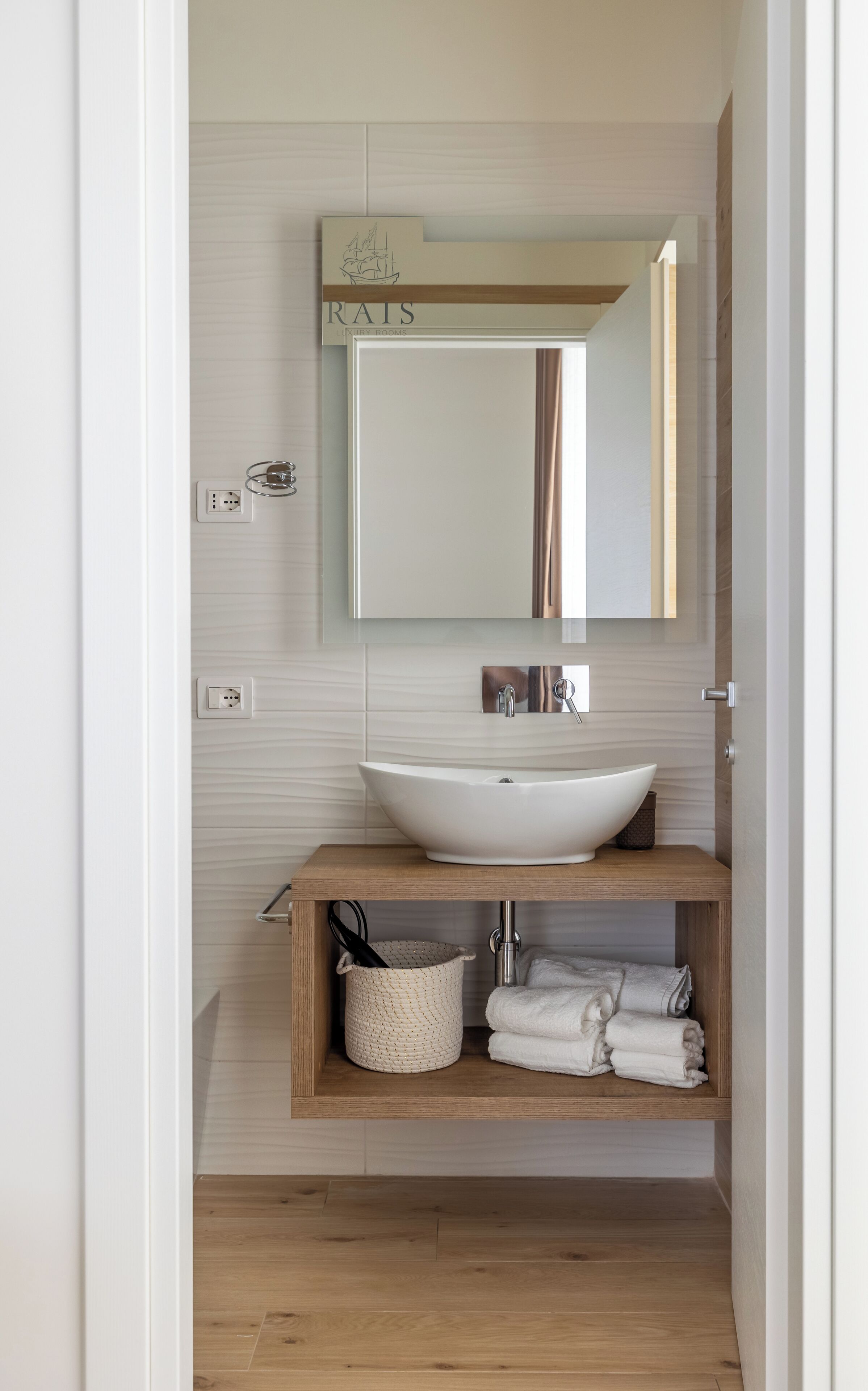 A bathroom with a white vessel sink, a wooden vanity, a mirror, and a towel rack.