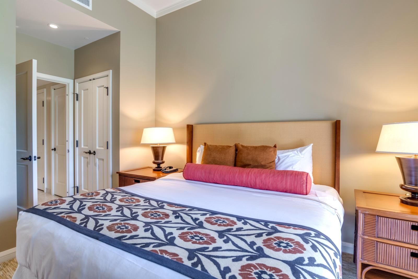 Une chambre d’hôtel avec un grand lit, deux tables de chevet avec des lampes et une porte donnant sur une autre pièce.