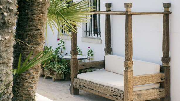 Un lit à baldaquin en bois, surmonté d’un matelas blanc, installé dans un espace extérieur aménagé en patio.