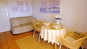 Een eethoek met een ronde tafel voor twee personen, een bank en rieten stoelen.