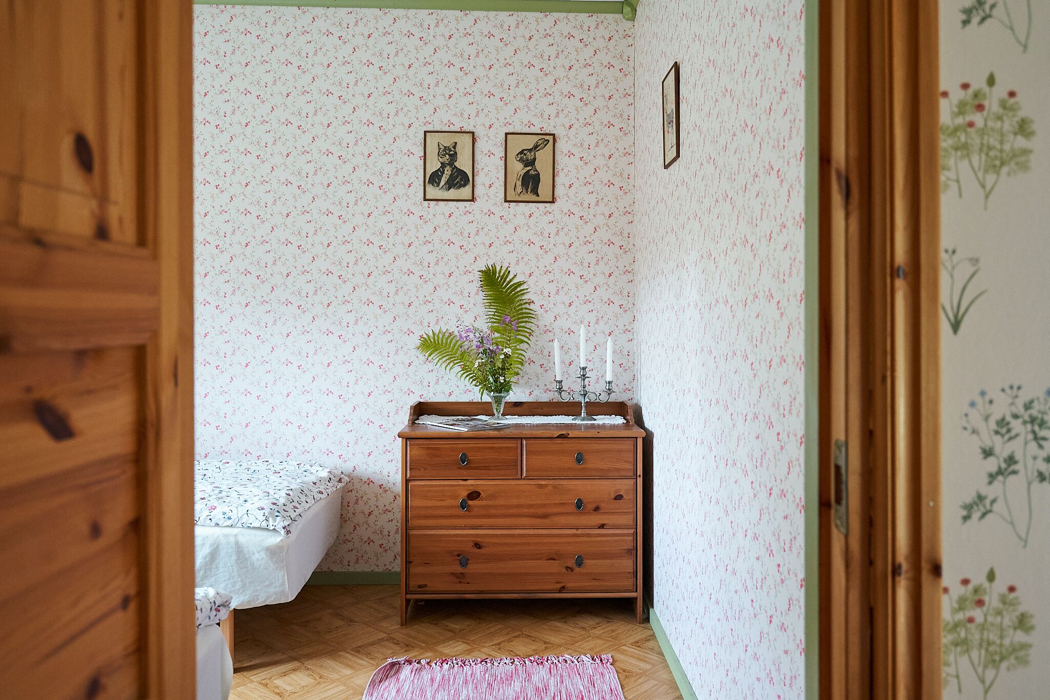 Ett rum med en byrå i trä, en säng med blommigt sänglinne och en liten krukväxt på byrån.