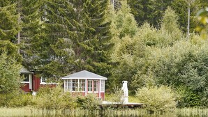 A tranquil lakeside setting with a small cabin and a statue. - Accommodation in the forest by the lake. Come and visit us in Sweden (Gunnarskog)