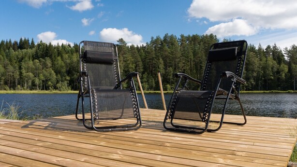 Two black chairs with mesh backs on a wooden deck by a lake. - Accommodation in the forest by the lake. Come and visit us in Sweden (Gunnarskog)