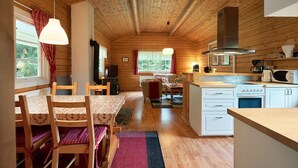 A cozy cabin-style kitchen with wooden walls, a dining area with a table and chairs, and a central seating area with a sofa and coffee table. - Accommodation in the forest by the lake. Come and visit us in Sweden (Gunnarskog)