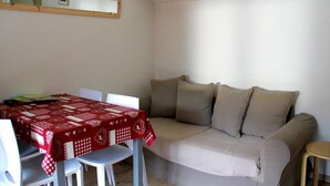 Ett rum med ett matbord täckt av en röd duk, en beige soffa och en liten pall.