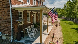 A brick building with a covered porch, outdoor seating, and American flags. - Wild Acres Farm, Fishery and Hunting Preserve - Lodge (Fredericktown)