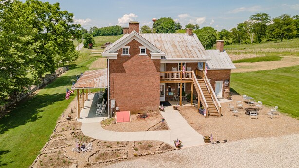 A two-story brick building with a balcony, a covered patio, and a gravel driveway. - Wild Acres Farm, Fishery and Hunting Preserve - Lodge (Fredericktown)