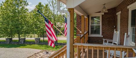 A wooden porch with a brick wall, a white railing, and two American flags.