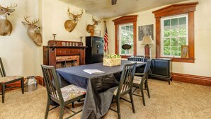 A dining room with a table set for four, surrounded by chairs. There are mounted deer heads on the wall, a ceiling fan, and a window with a view of greenery. - Wild Acres Farm, Fishery and Hunting Preserve - Lodge (Fredericktown)