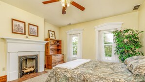 A bedroom with a fireplace, a bed with camouflage bedding, a wooden dresser, and a large green plant. - Wild Acres Farm, Fishery and Hunting Preserve - Lodge (Fredericktown)
