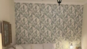En moderne stue med en hjørnesofa, tapet med et mønster, en hængende lampe og et lille natbord.