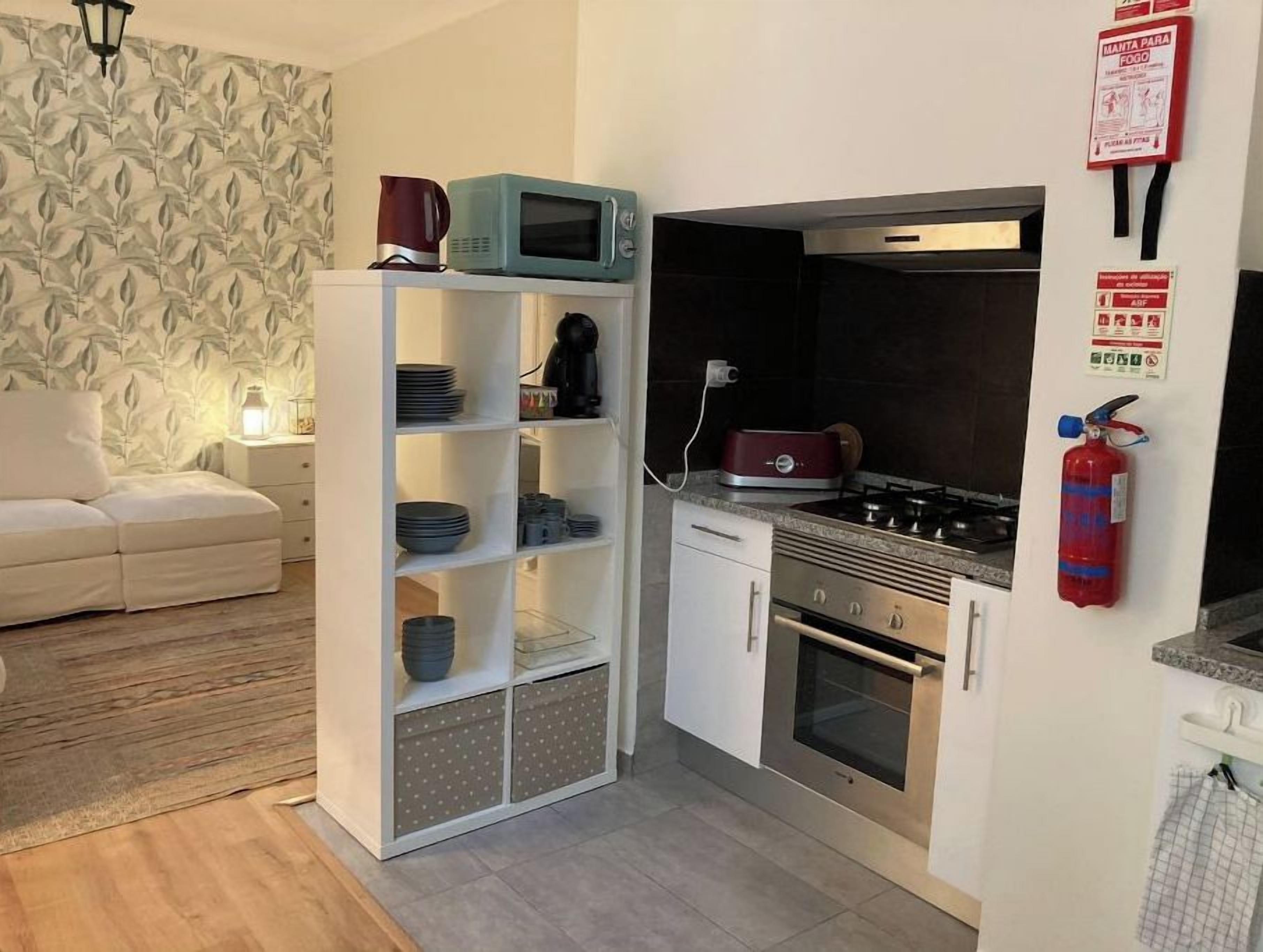 A compact kitchen with white cabinets, a microwave, a stove, and a fire extinguisher.
