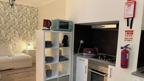 Una cocina compacta con armarios blancos, un microondas, una estufa y un extintor.