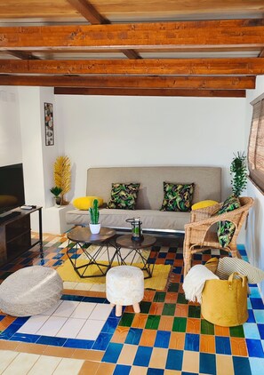 Un salon comprenant un canapé, une table basse, un pouf et un fauteuil en osier.
