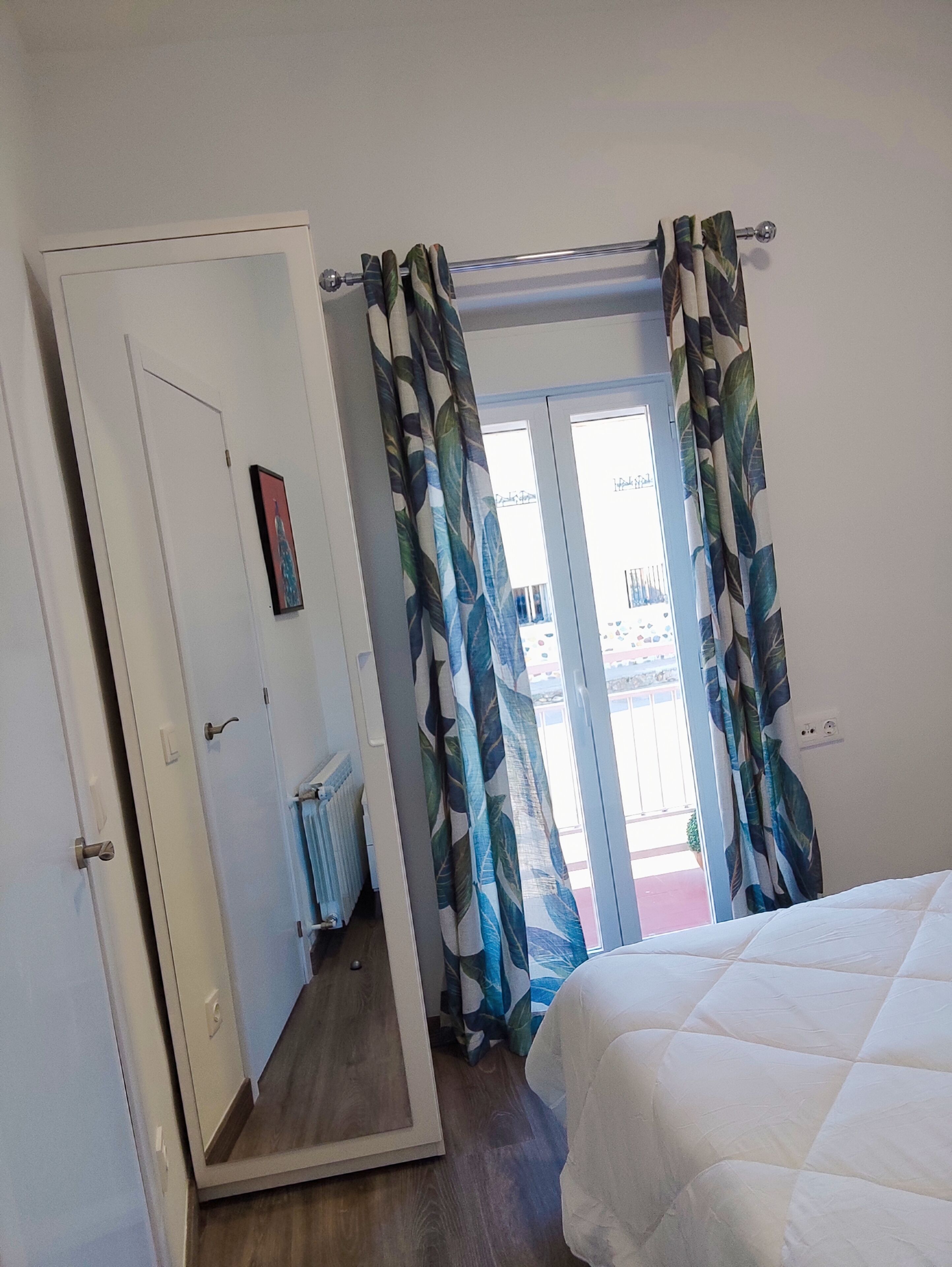 Une chambre à coucher avec un lit, une porte, un radiateur et une fenêtre avec des rideaux.