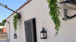 A white wall with a black door, green plants, and two lantern-style lights. - Cozy, bright, terrace-solarium, rustic living room. Very close to Madrid... (Villarejo de Salvanés)