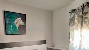 A bedroom with two beds, a headboard, a wall-mounted artwork, a bedside table, and a curtain with a leaf pattern. - Cozy, bright, terrace-solarium, rustic living room. Very close to Madrid... (Villarejo de Salvanés)