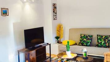 Een woonkamer met een televisie, bank, kleurrijke vloertegels en een houten plafond.