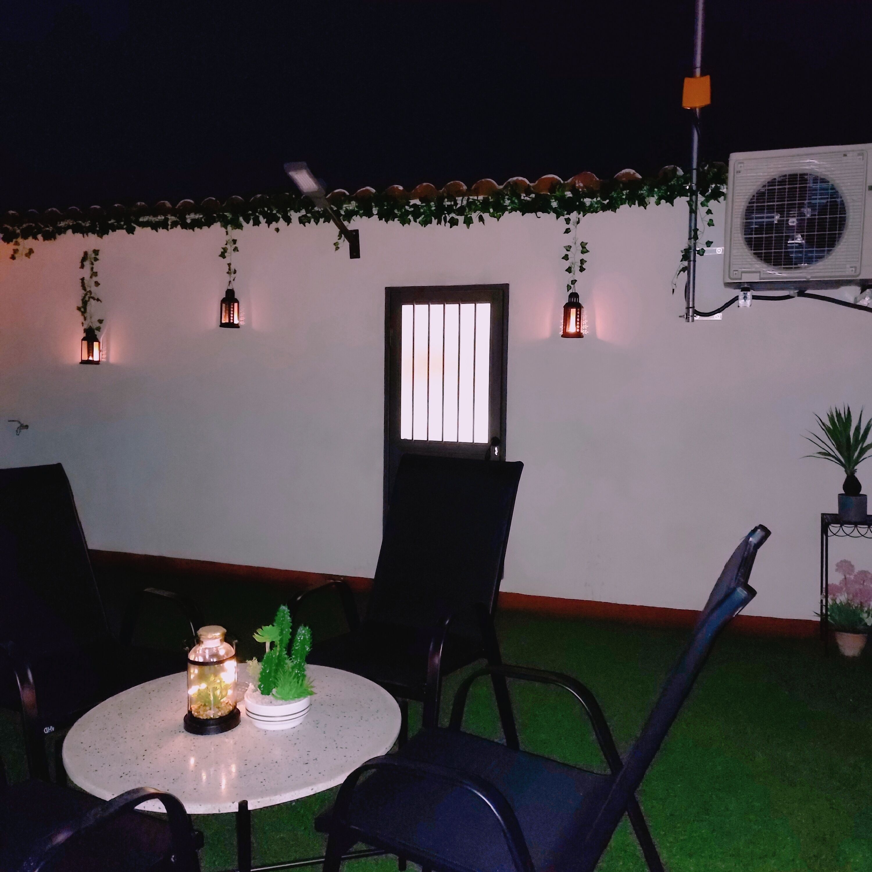 Un área de estar al aire libre con una mesa redonda, sillas y faroles decorativos.