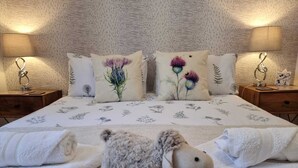 A neatly made bed with floral bedding, two bedside lamps, and a plush toy on the bed. - HEART OF INVERNESS MODERN APARTMENT (Inverness)