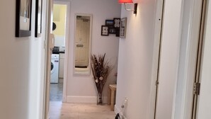 A hallway with a wooden floor, white walls, and a ceiling light. There are framed pictures on the wall, a radiator, and a door on the right. - HEART OF INVERNESS MODERN APARTMENT (Inverness)