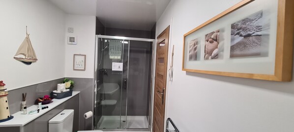 Ett modernt badrum med en duschkabin i glas, ett handfat med hygienartiklar och en inramad tavla på väggen.