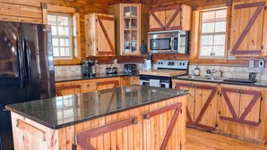 Una cocina con armarios de madera, un refrigerador negro, un microondas, una estufa y un lavamanos.