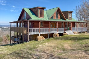 A log cabin with a green roof, a porch, and a view of the landscape. - Best View in Heber Springs | Mountain Cabin for 12 (Heber Springs)