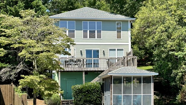 A two-story house with a deck and a covered area, surrounded by water and greenery. - Premier Waterfront Location! Big, clear water views! Fire table! (Dadeville)