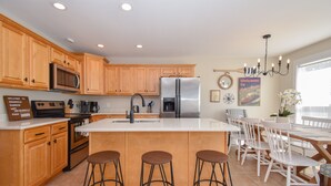 A modern kitchen with wooden cabinets, stainless steel appliances, a large island with stools, and a dining area with white chairs. - Premier Waterfront Location! Big, clear water views! Fire table! (Dadeville)