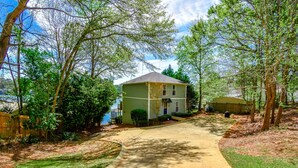 A residential property with a paved driveway leading to a house, surrounded by trees and a fenced yard. - Premier Waterfront Location! Big, clear water views! Fire table! (Dadeville)
