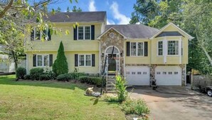 A two-story house with a stone front, a garage, and a well-maintained lawn. - Chandler Retreat - Lakehouse (Acworth)