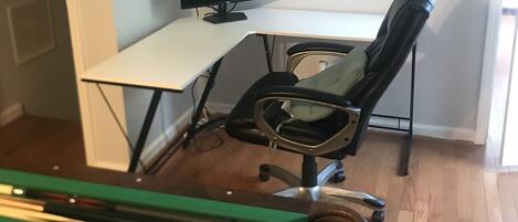 Una habitación con mesa de billar, escritorio con silla y ventana.