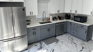 A modern kitchen with white cabinets, a stainless steel refrigerator, a microwave, and a coffee maker. - Chandler Retreat - Lakehouse (Acworth)