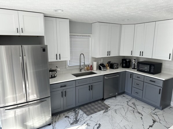A modern kitchen with white cabinets, a stainless steel refrigerator, a microwave, and a coffee maker.