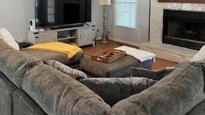 A living room with a large gray sectional sofa, a flat-screen TV, a fireplace, and a ceiling fan. - Chandler Retreat - Lakehouse (Acworth)