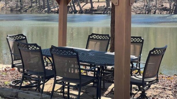 A covered outdoor seating area with a table and chairs overlooking a lake. - Chandler Retreat - Lakehouse (Acworth)