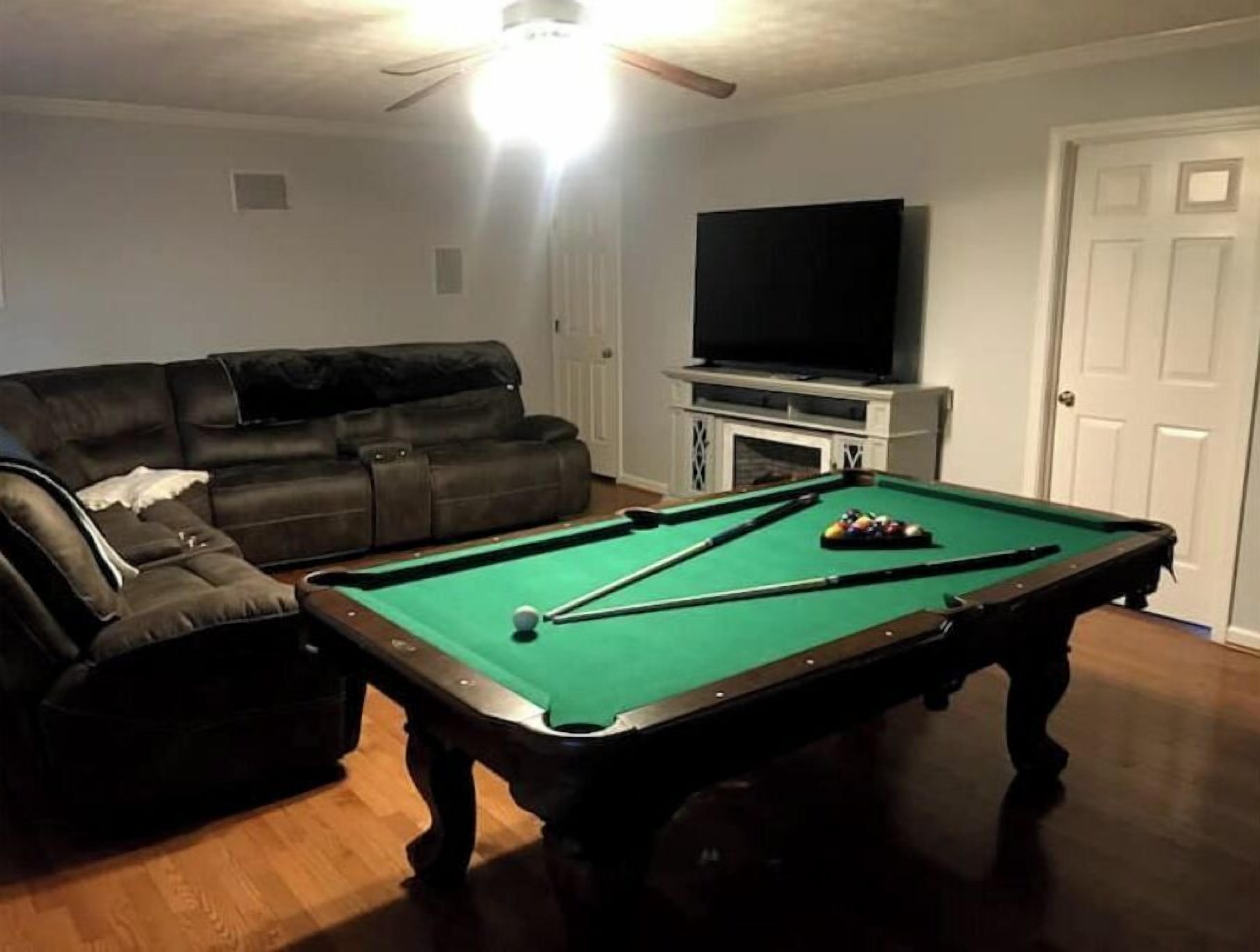 A living room with a pool table, a sofa, a television, and a fireplace.