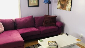 En stue med en lilla sofa, et hvidt sofabord og en gulvlampe.