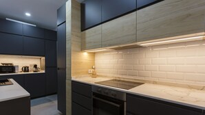 Une cuisine moderne avec des meubles de couleur sombre, un plan de travail en marbre blanc et un four encastré.
