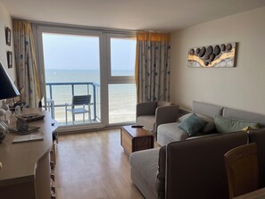 A living room with a sofa, a chair, a table, and a view of the sea through large windows.