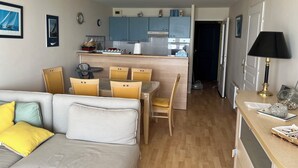 A compact living space with a dining area, kitchenette, and a sofa with cushions. - Apartment with sea view (Bray-Dunes)