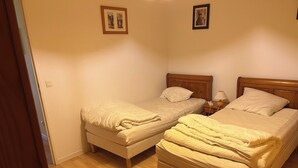 A bedroom with two single beds, wooden headboards, a nightstand with a lamp, and a wooden floor. - Apartment with sea view (Bray-Dunes)